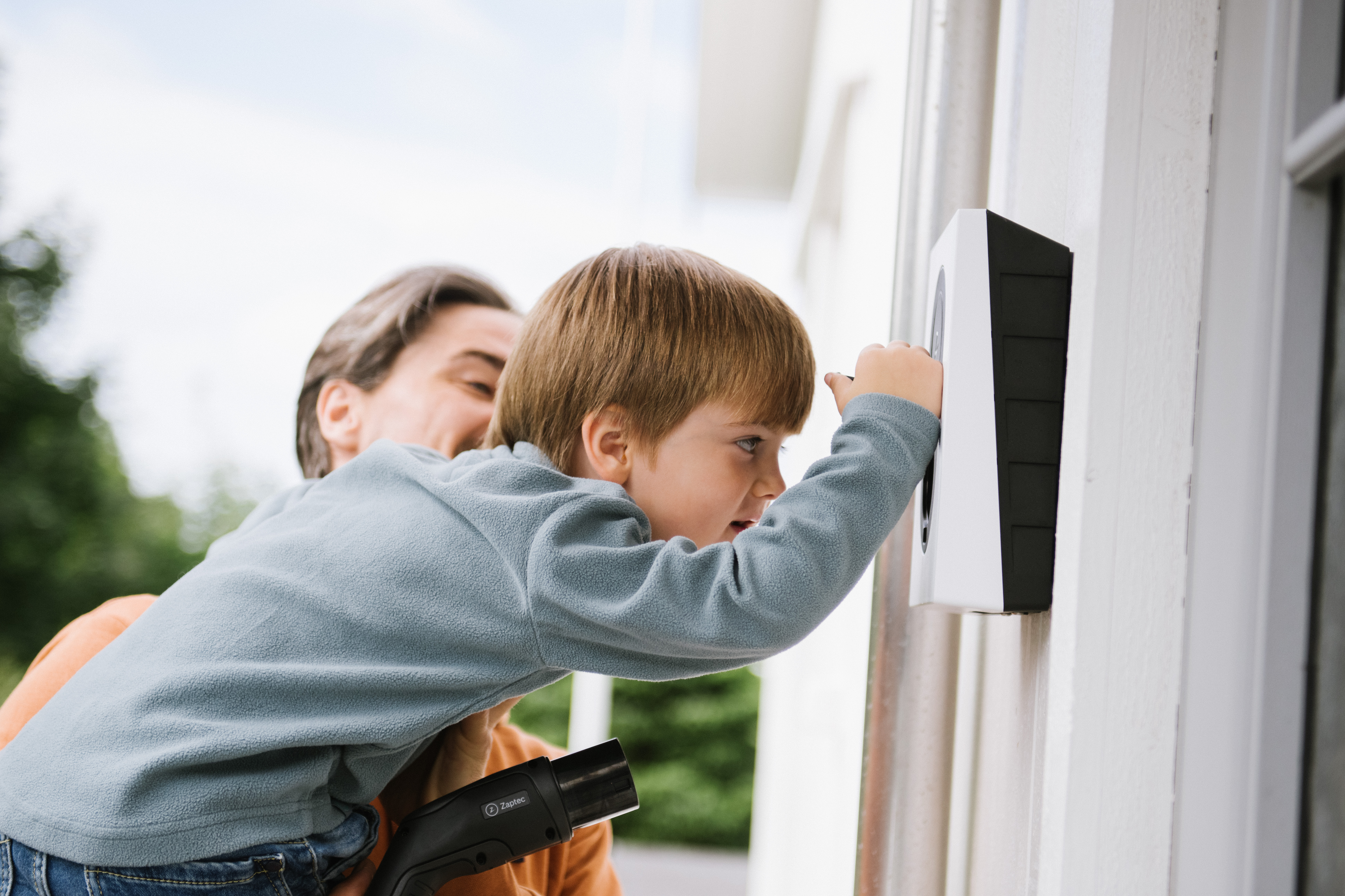 Far med barn, der undersøger en zaptec go ladeboks på væggen af deres hus - nyhed om prøvekunder til zaptec ladeboks
